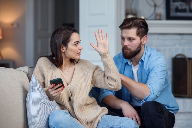 woman holding smartphone while sitting near man