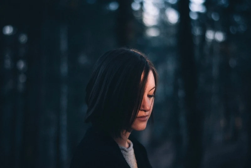 woman in black coat standing in forest