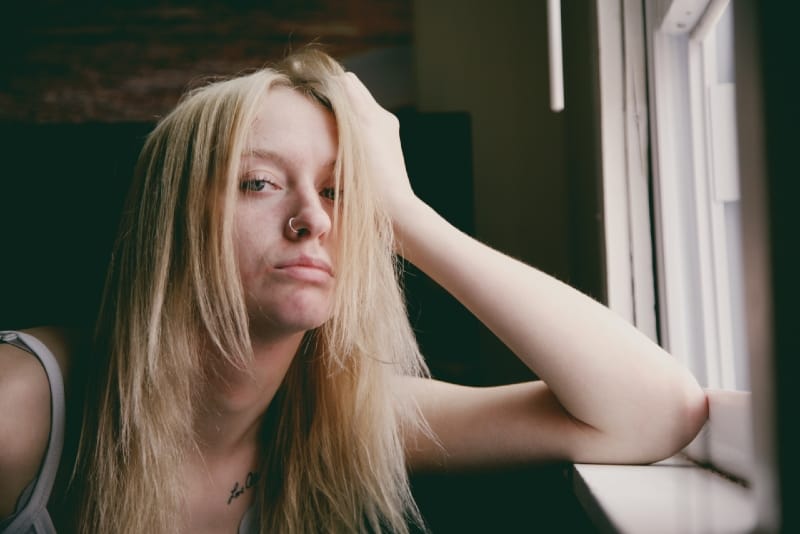 mujer rubia con aro en la nariz apoyada en el cristal de la ventana