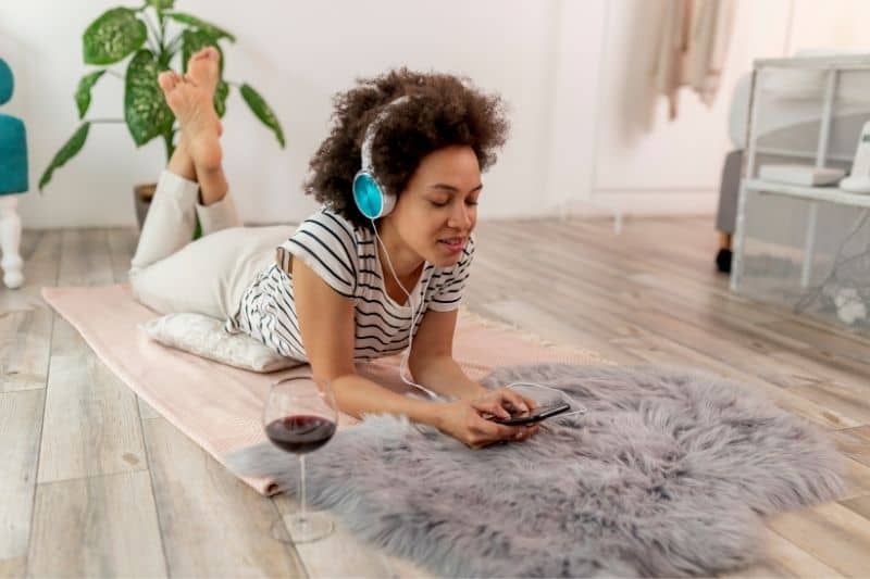 donna che impara una nuova lingua online ascoltando attraverso le cuffie guardando lo smartphone un vino sul lato