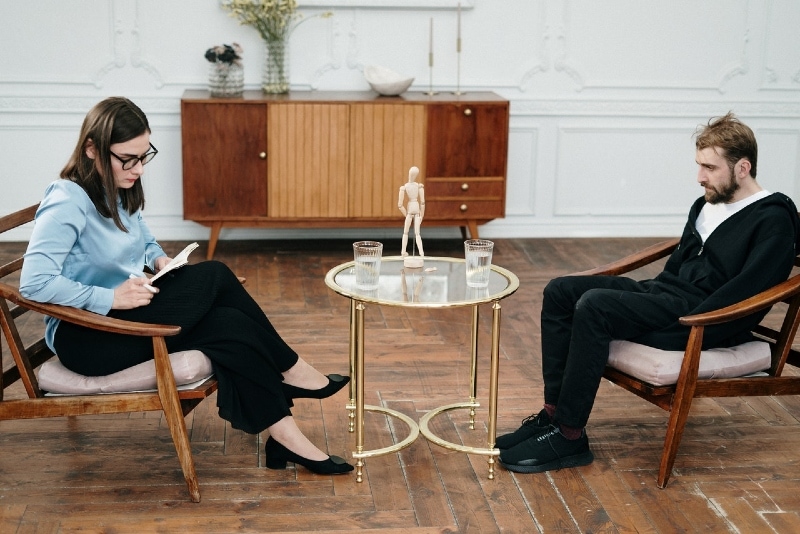 woman looking at notebook while sitting on chair near man