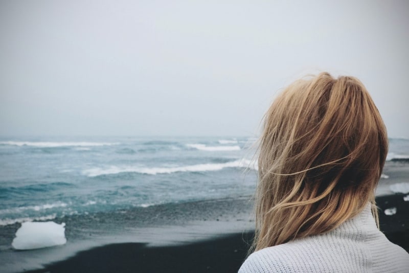 mujer rubia con jersey blanco mirando al oceano