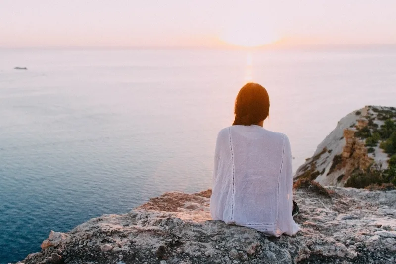 woman looking at sunset while sitting on rock