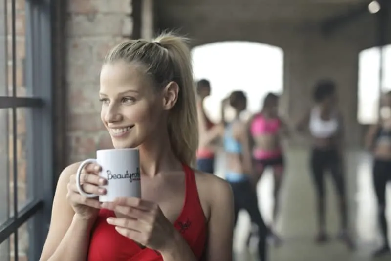 woman looking through window while holding white ceramic mug