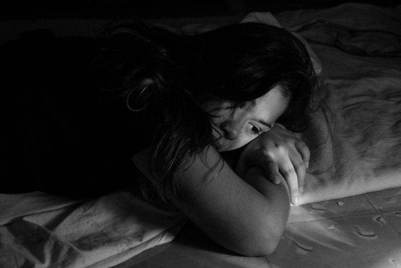 donna triste con maglietta nera sdraiata sul letto