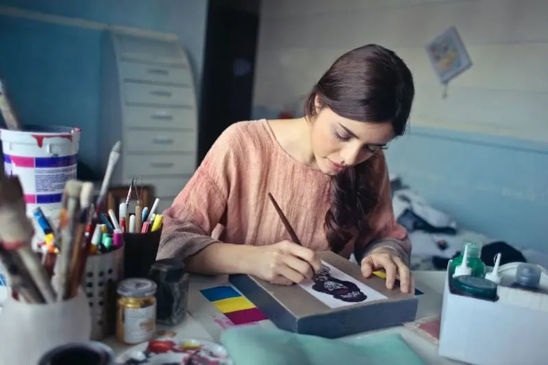 woman in brown blouse painting while sitting at table