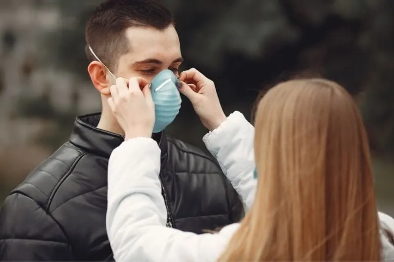 woman putting facemask on a man outdoors