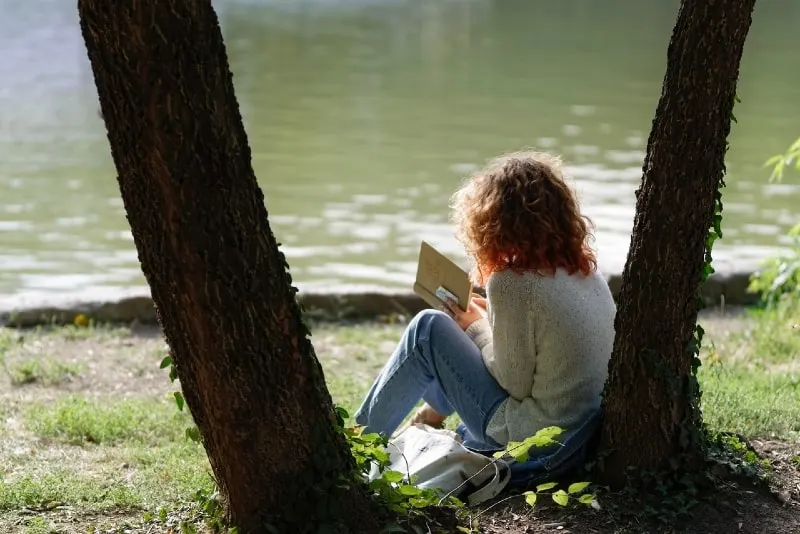 woman reading a book while sitting near tree
