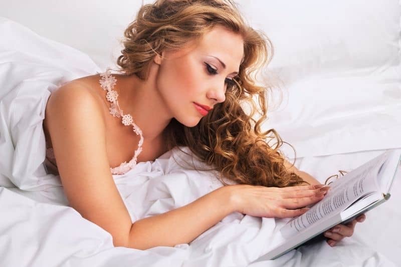donna che legge un libro a letto coprendosi con una coperta a letto