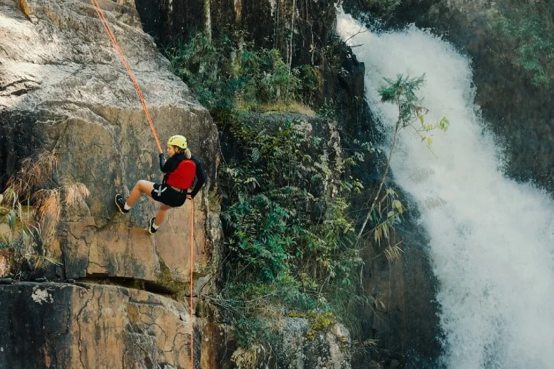woman rock climbing near waterfall