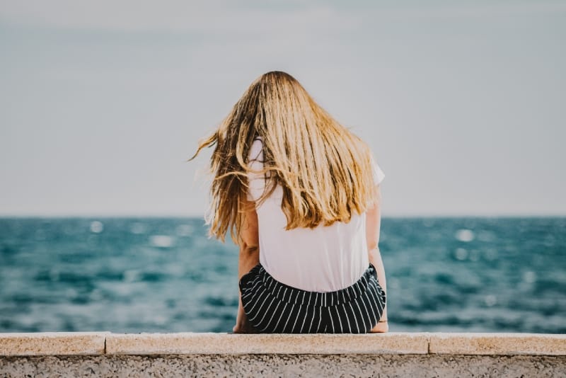 mujer con camiseta blanca sentada cerca del mar