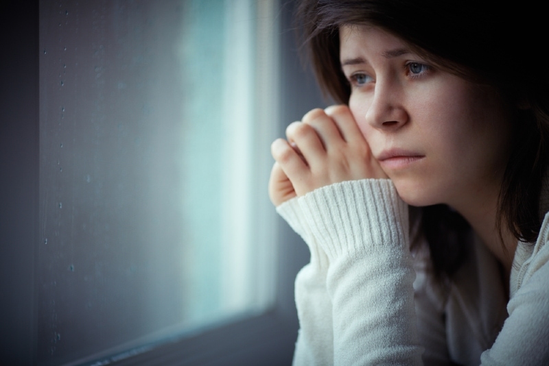 sad woman in white sweater sitting near window