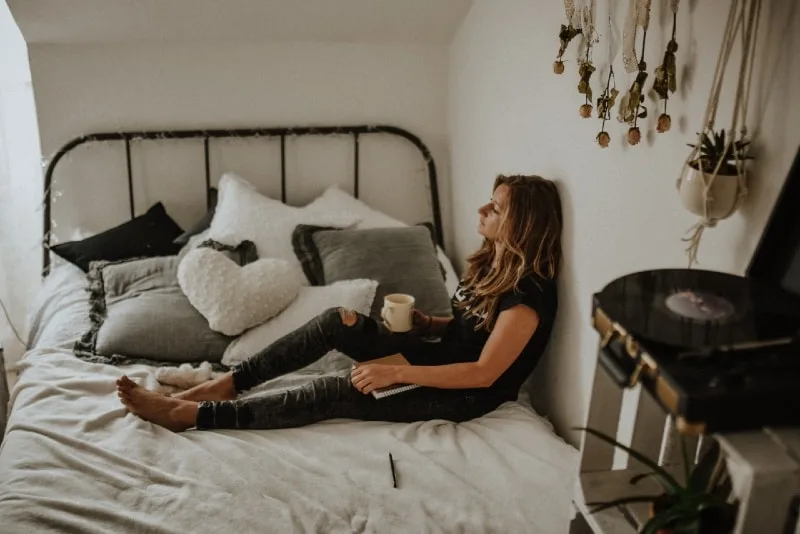 woman holding white mug while sitting on bed