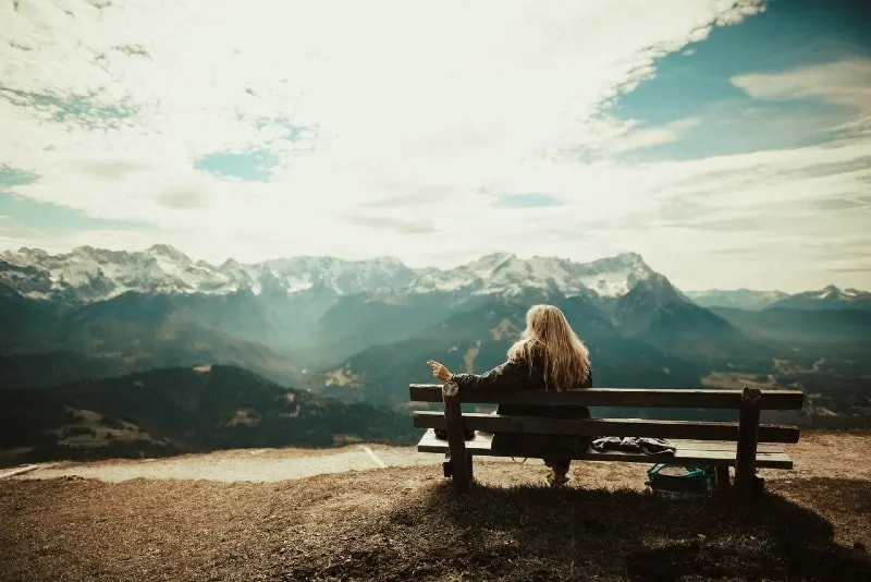 blonde woman sitting on bench looking at mountain