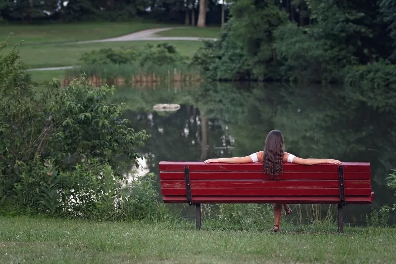 woman sitting on red bench looking at water