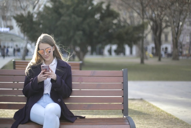 mulher sentada num banco enquanto utiliza um smartphone