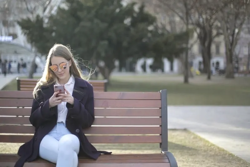 woman sitting on bench while using smartphone