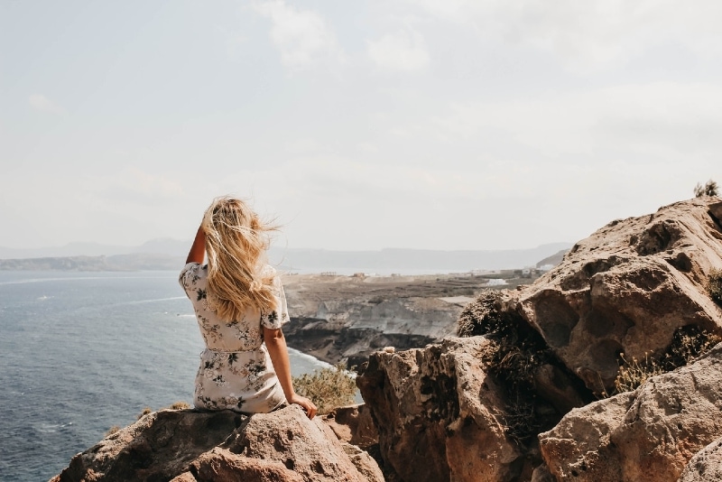 woman sitting on cliff looking at sea