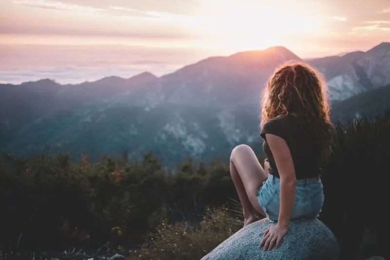 woman sitting on rock looking at mountain