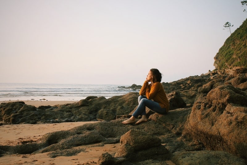 woman in yellow sweater sitting on rock