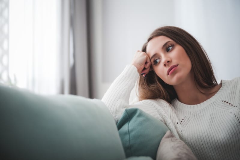 sad woman in white sweater sitting on sofa