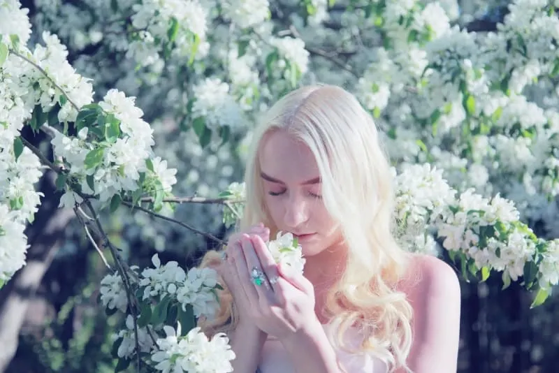 blonde woman smelling flower during daytime