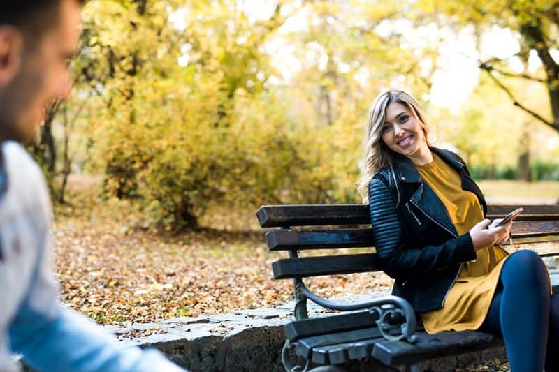 donna che sorride a uno sconosciuto seduto su una panchina nel parco