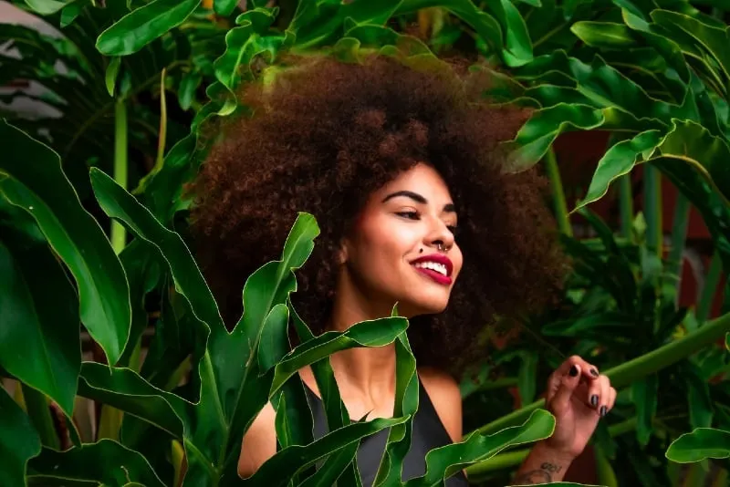 happy woman with curly hair standing near plants