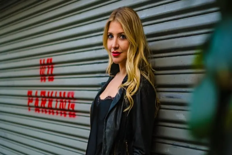 blonde woman in black jacket standing near shutter door