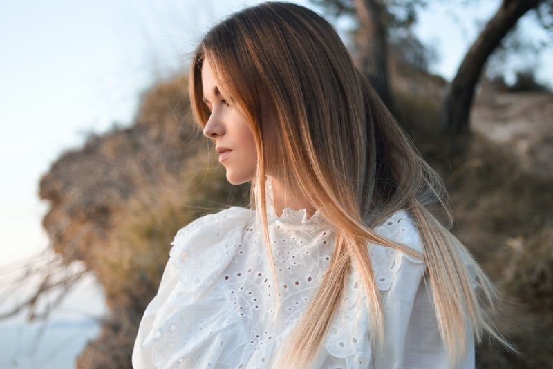 woman in white top standing near trees