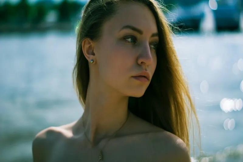 woman with golden necklace standing near water