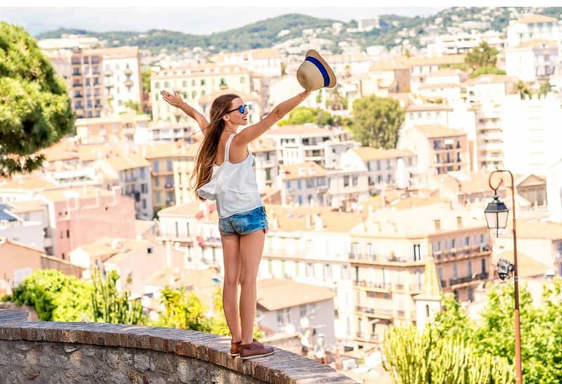 woman standing on a ledge raising her hands overlooking the city