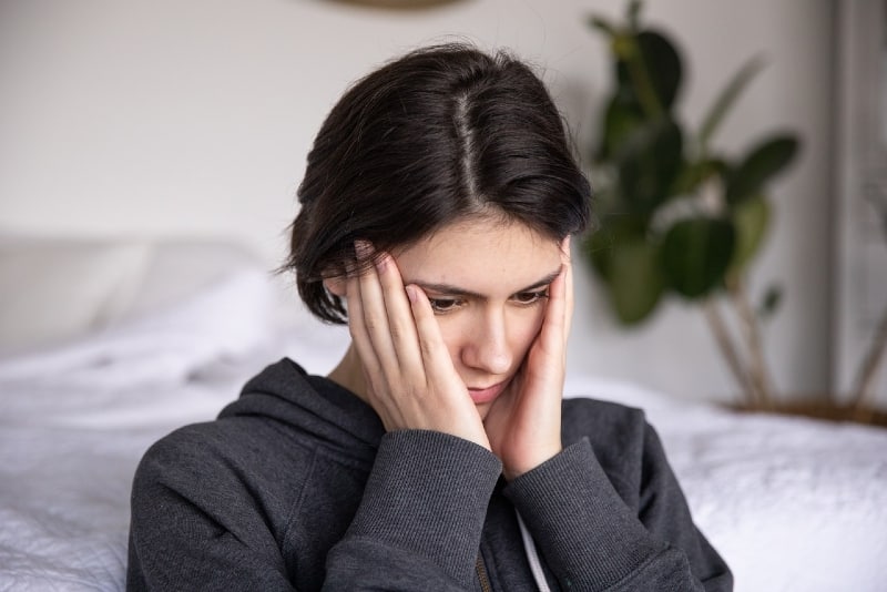 woman touching her face while sitting near bed