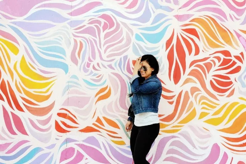 woman touching her hair while standing near colorful wall