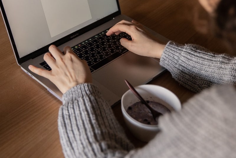 woman in gray sweater using laptop during meal