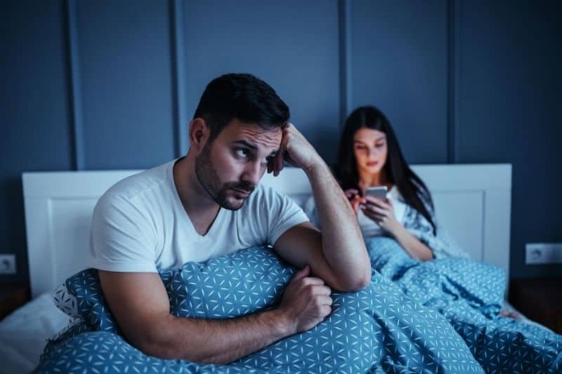 woman using smartphone ignoring her bored husband in bed