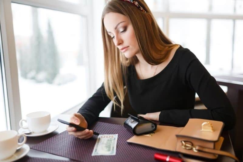 mujer esperando mensaje de texto o llamada desde smartphone sentada junto a mesa en interior