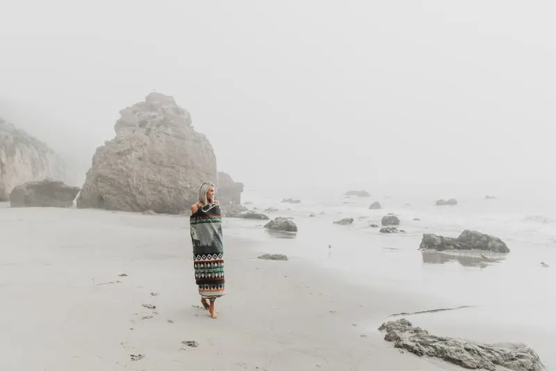 woman wrapped in blanket walking on seashore