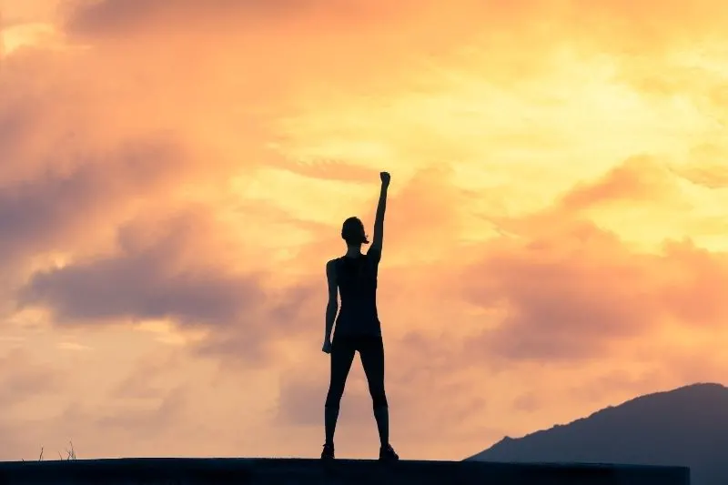 woman with fist in the air standing up with hope and courage during dusk/dawn