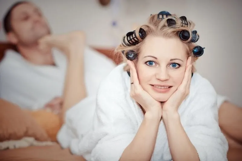 woman with hair rollers lying on bed with foot at the man's chin