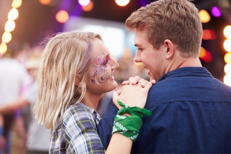 woman with painted face hugging on a man ourdoors while watching a concert