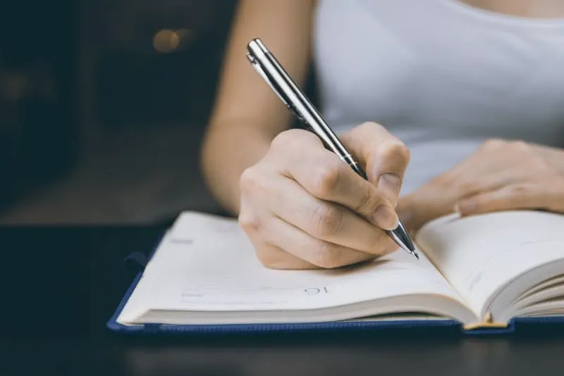woman writing with pen on notebook