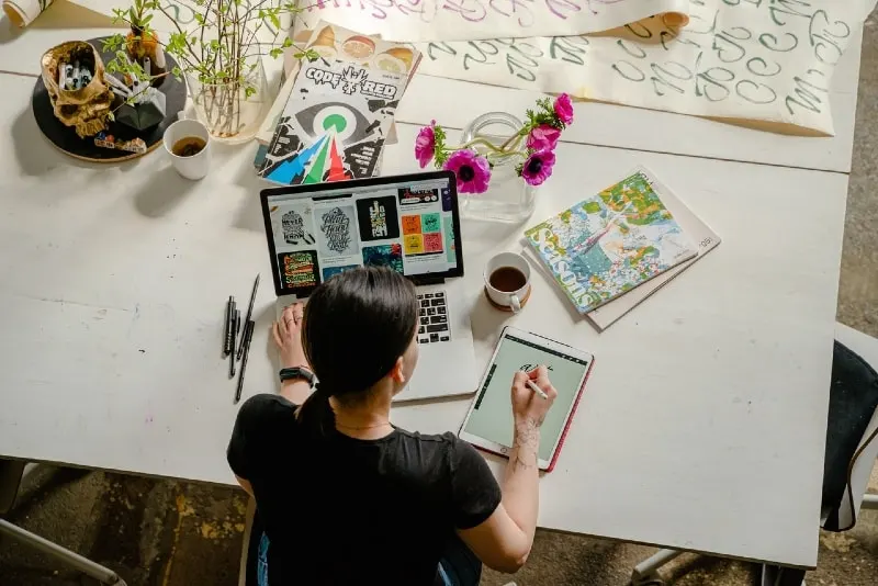woman writing on tablet while using laptop
