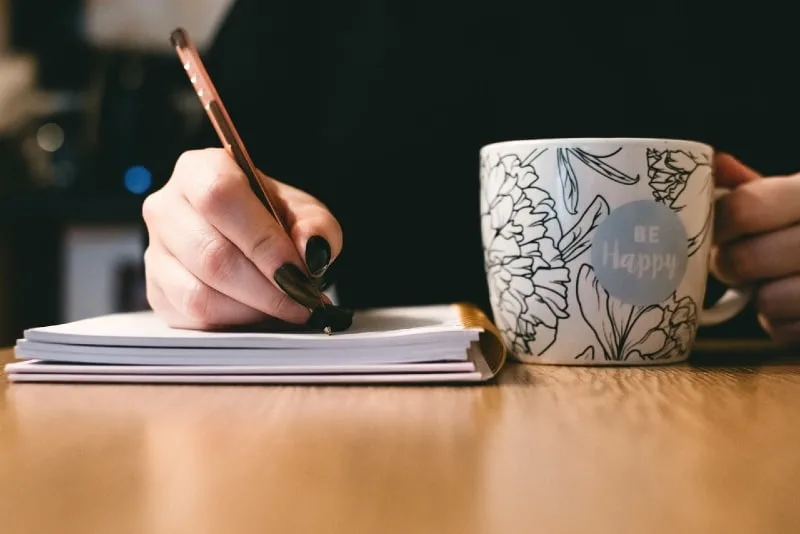 woman writing while holding ceramic mug