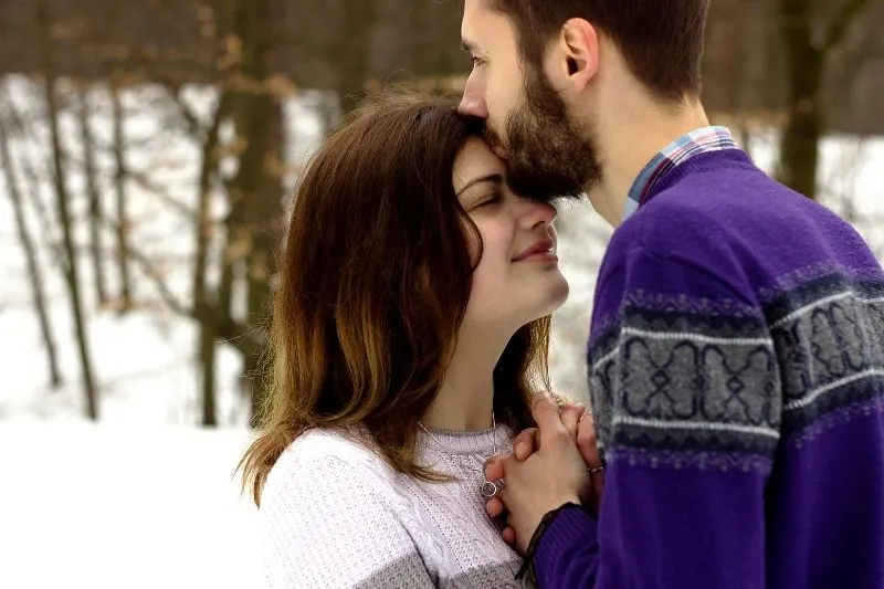 woman's forehead kissed by a man standing outdoors during winter