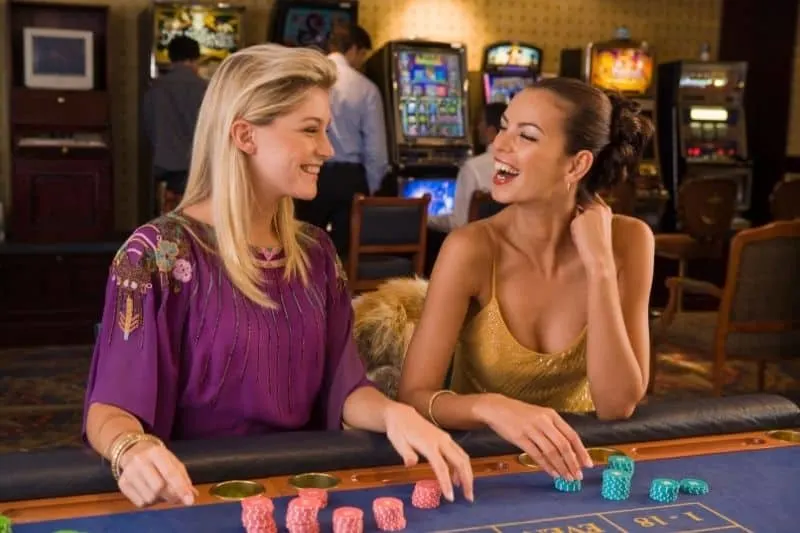 women gambling in casino laughing while sitting by the game board