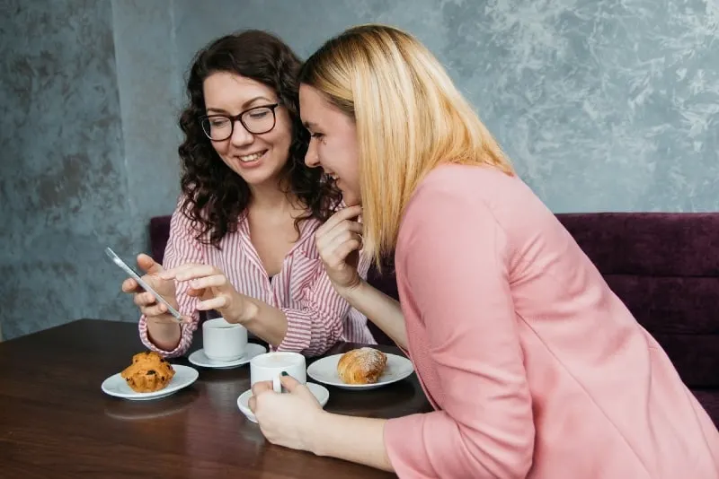 two women looking at phone while sitting at table