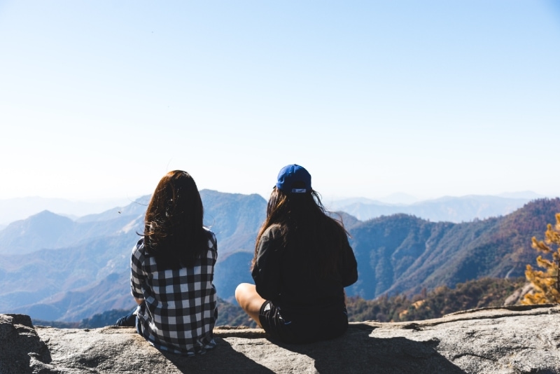two women sitting on rock looking at mountain
