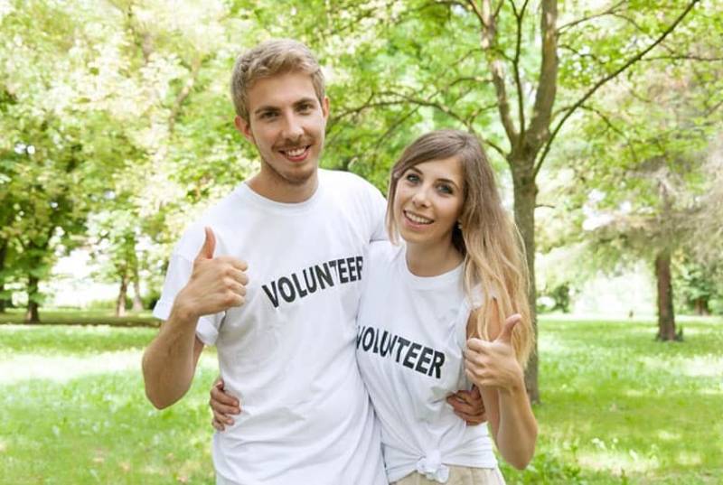 young couple volunteers hugging with hand sign of approval standing outdoors