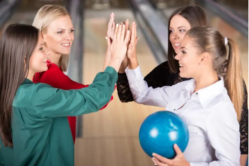 young group of female friends doing high five during a bowling game indoors